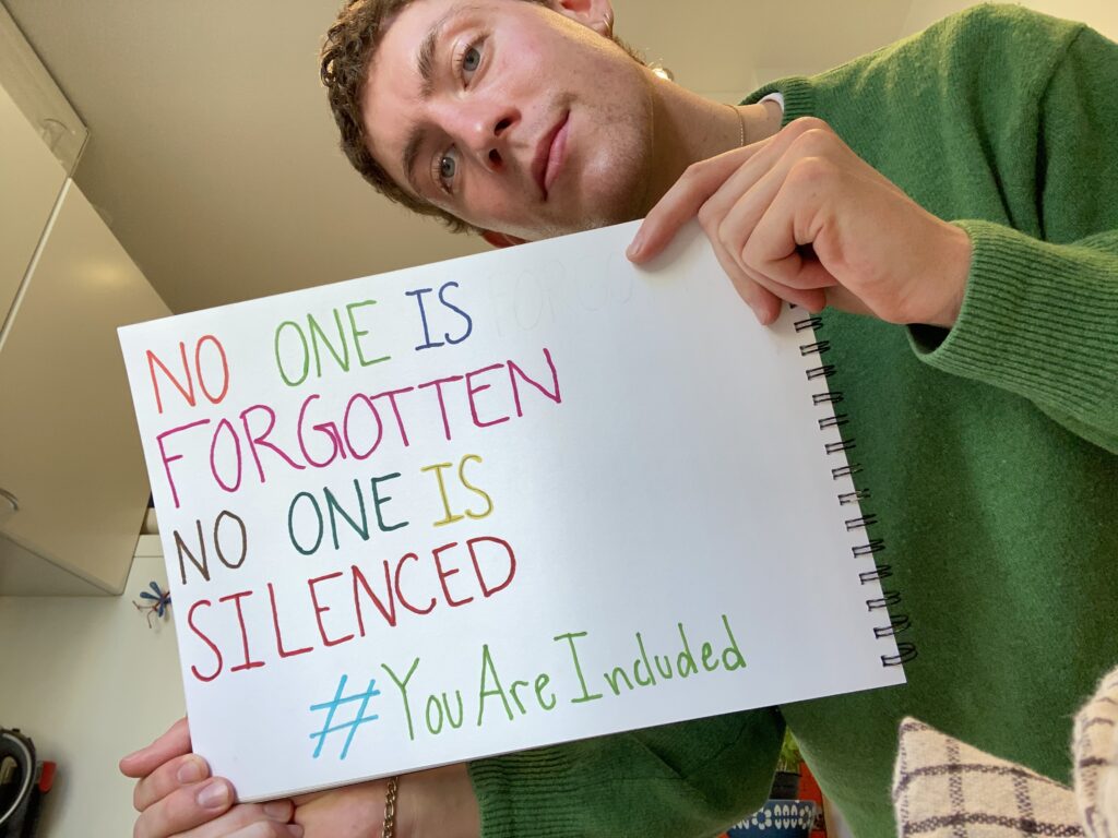 Guy holding up a sign saying: No one is forgotten, no one is silenced. #YouAreIncluded
